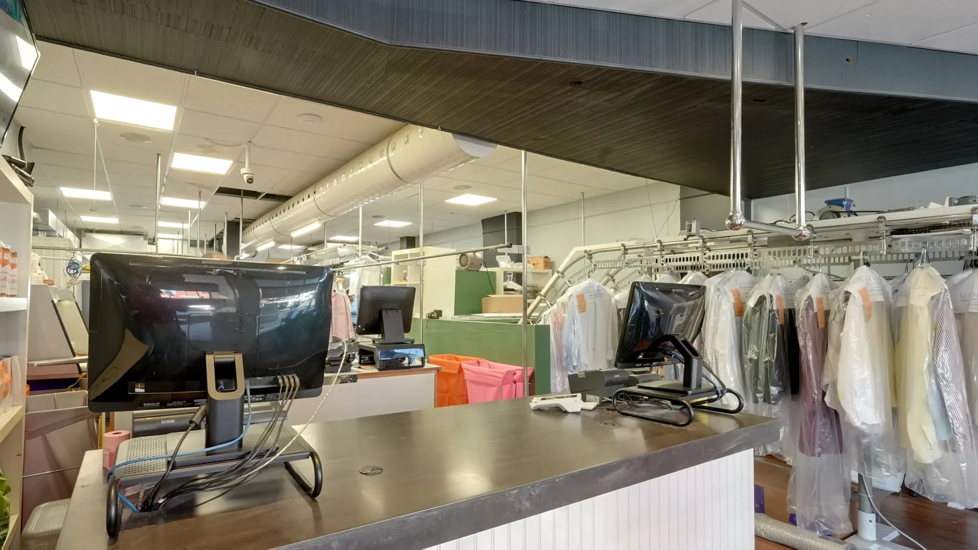 The front counter seen from the customer side, with garments in clear covers on the conveyor behind it