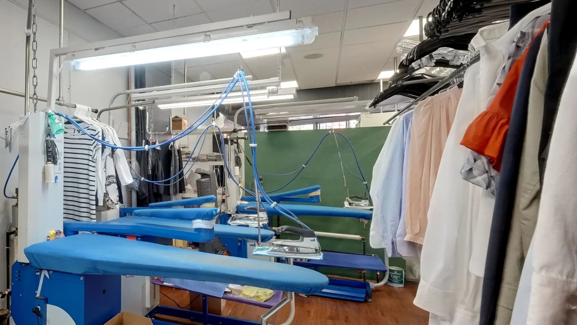 Blue padded ironing boards and steam irons in the shirt room, with dress shirts hanging on the rail